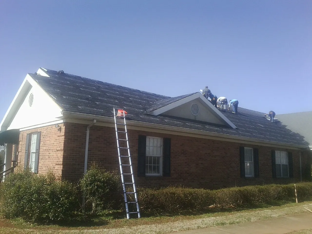 Crew tearing shingles off a brick ranch roof with a ladder set — Metal Roof Repair work by our crew in New Holland