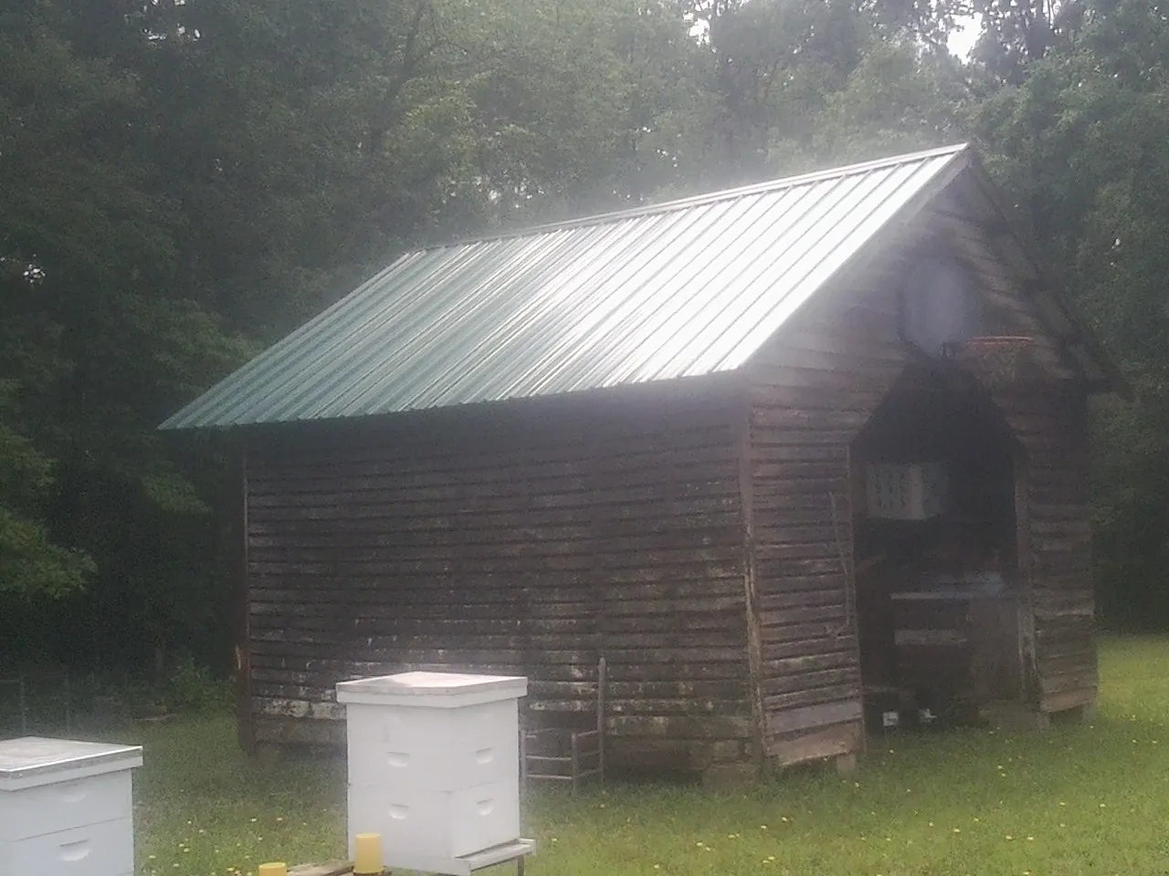 Green metal roof on a weathered barn beside stacked beehives in New Holland