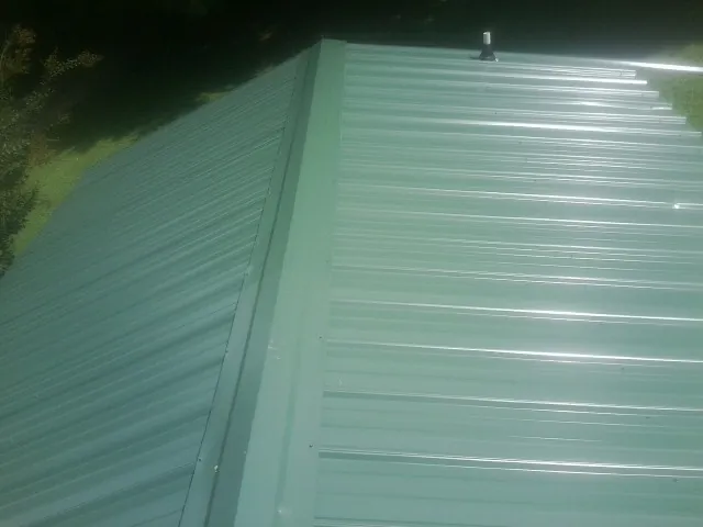 New green metal panels meeting at the ridge of a roof — Flat Roof Repair work by our crew in New Holland