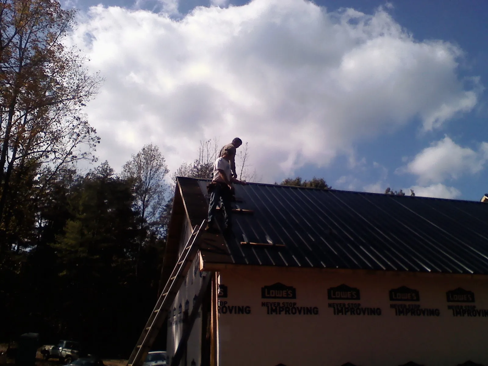 Roofer fastening dark metal panels high against a cloudy sky, from a Roof Inspection job in New Holland